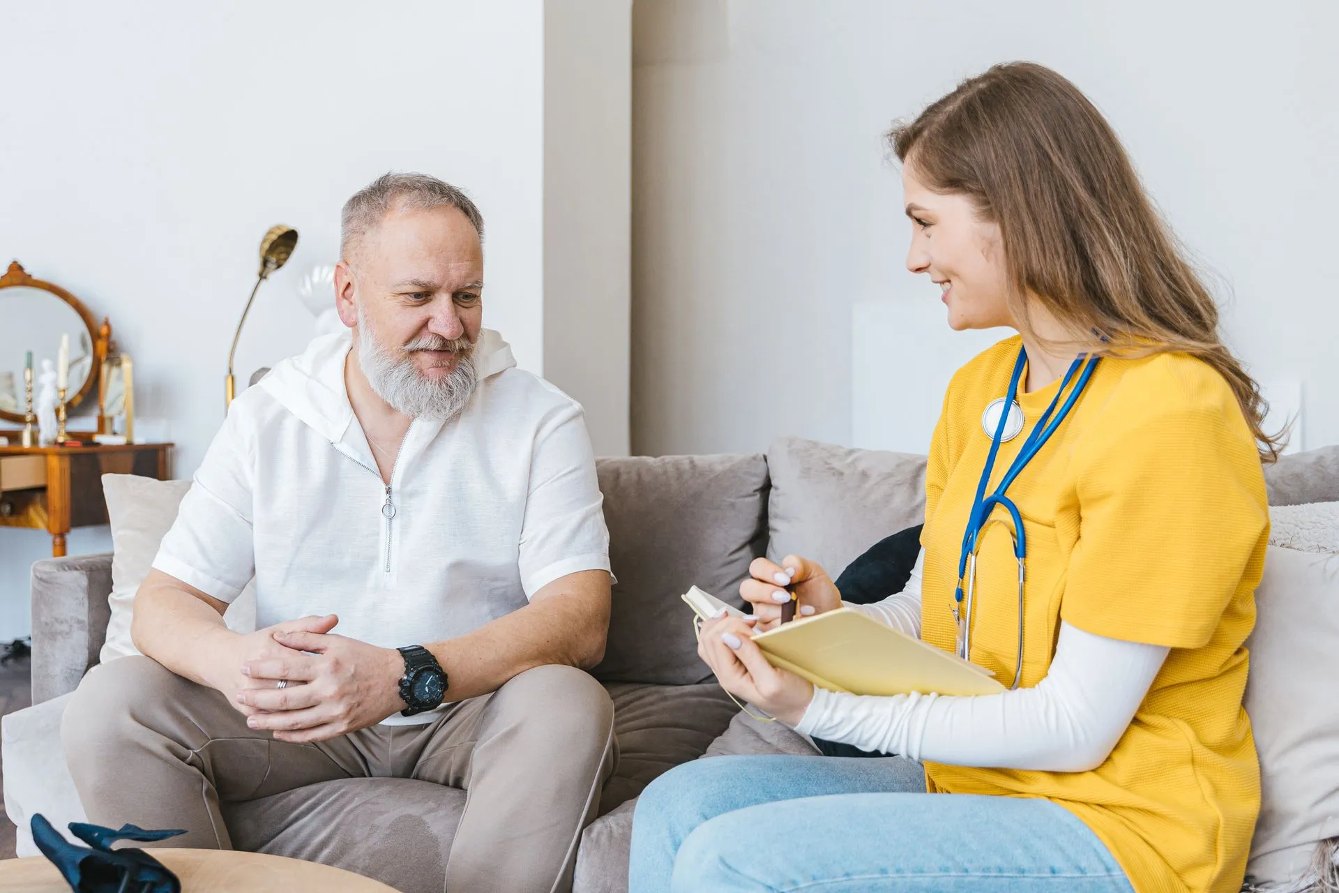 Una enfermera de salud en el hogar conversando con un paciente mayor sonriente en casa